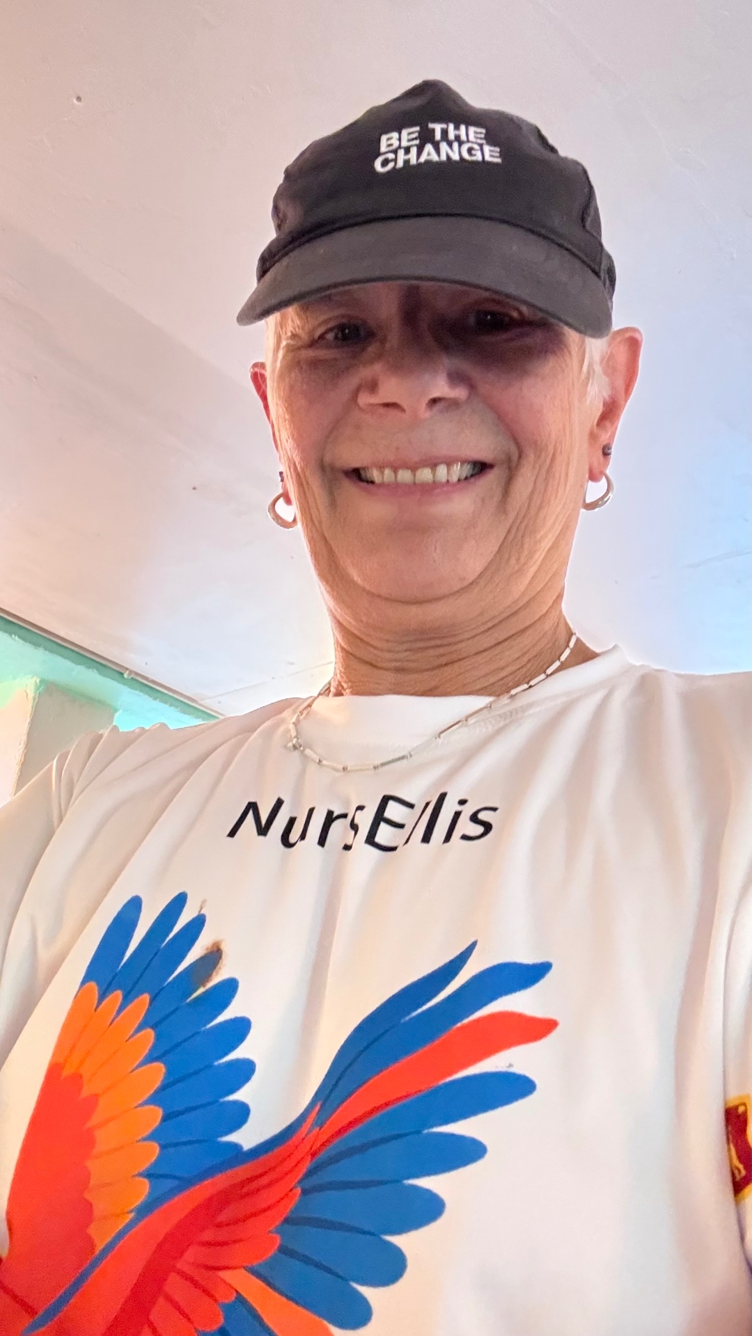 Nurs Ellis smiling, wearing a Nurs Ellis t-shirt with a phoenix wing print and a Be The Change cap